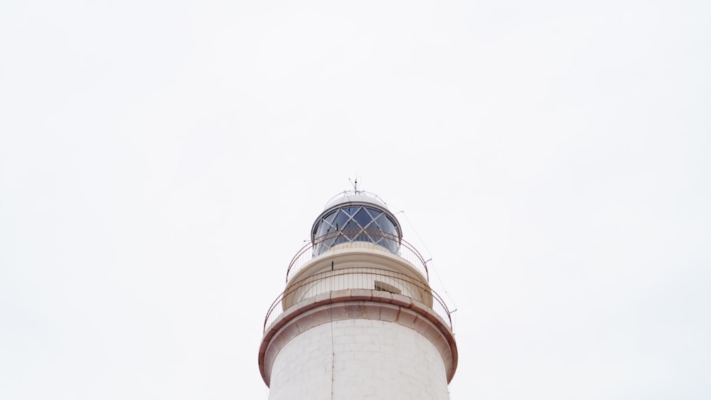 low-angle photography of white lighthouse under white clouds