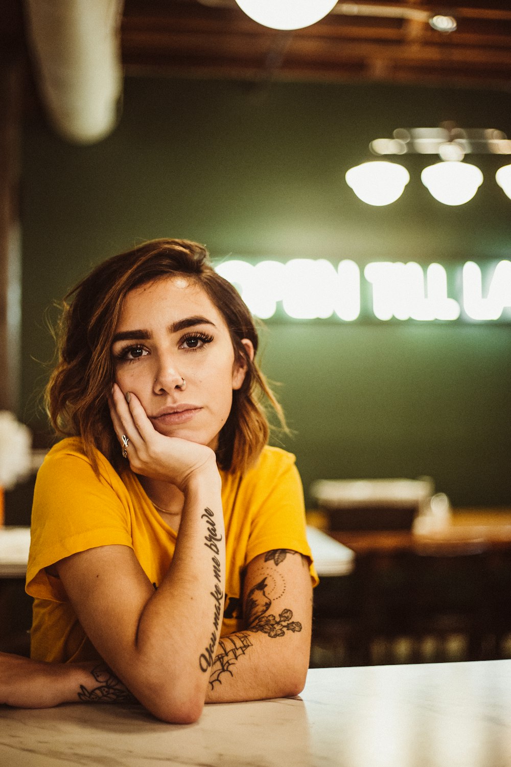 woman wearing yellow crew-neck shirt sitting beside table posing for photo