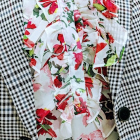 A close-up of a garment featuring a houndstooth checkered pattern next to a floral print with ruffled fabric. The floral pattern includes red and pink flowers with green leaves, creating a contrast against the black and white texture.