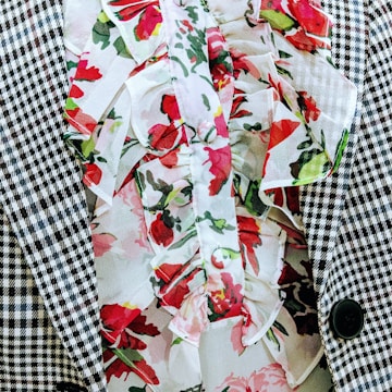 A close-up of a garment featuring a houndstooth checkered pattern next to a floral print with ruffled fabric. The floral pattern includes red and pink flowers with green leaves, creating a contrast against the black and white texture.