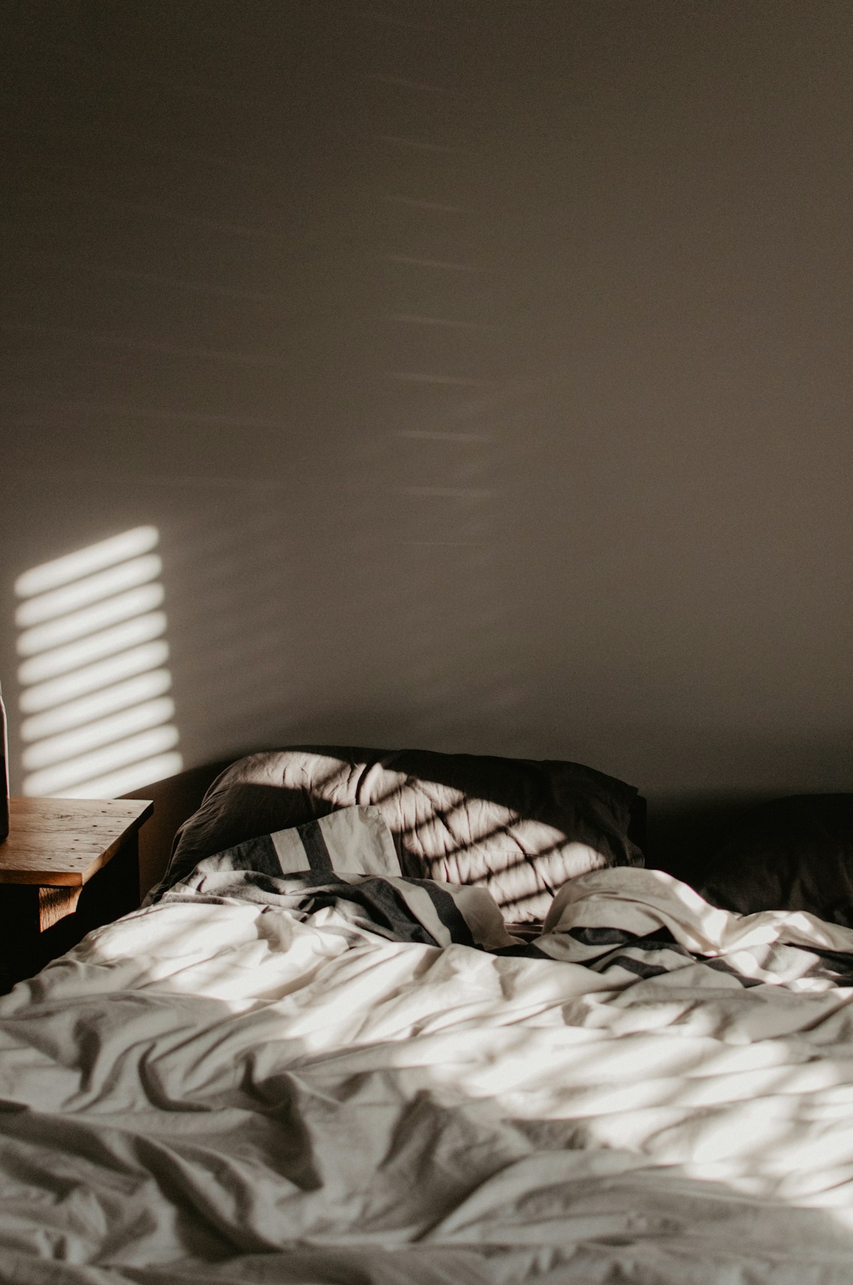 Sunlit bedroom with rumpled white linen sheets catching morning light through the blinds