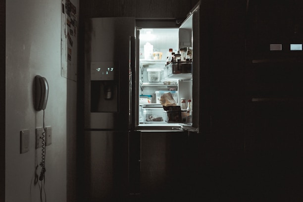 Technician repairing a refrigerator inside a modern kitchen setting.