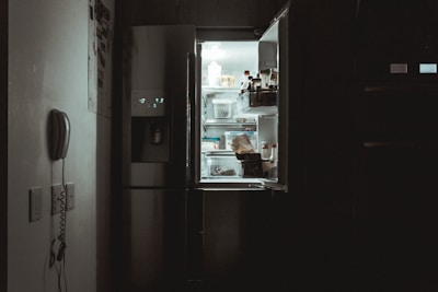 Technician carefully repairing a modern refrigerator inside a bright kitchen.