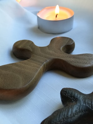 A close-up of a prayer card resting gently on a wooden table beside a softly glowing candle.