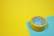 A roll of yellow adhesive tape sits on a yellow and blue surface. The tape has text on the inside.