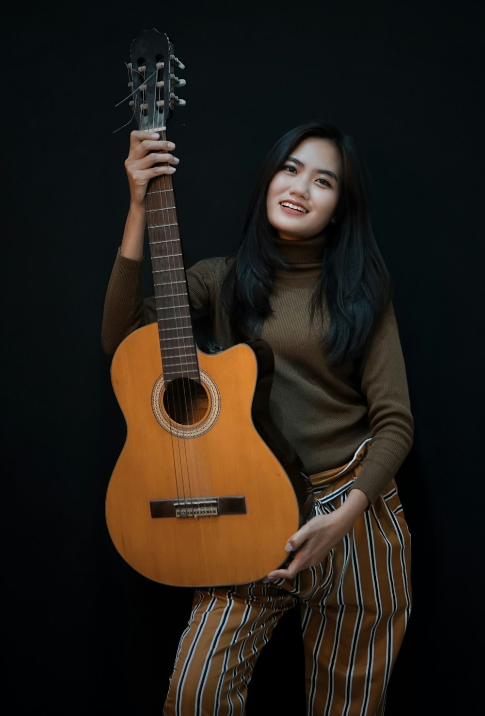 smiling woman while holding cut-away acoustic guitar