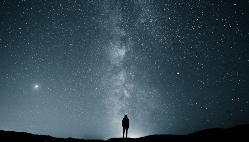 A lone figure silhouetted against a star-filled night sky