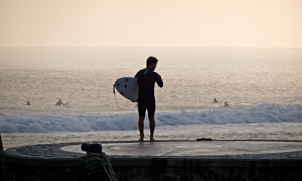 Homem segurando prancha de surf perto da costa