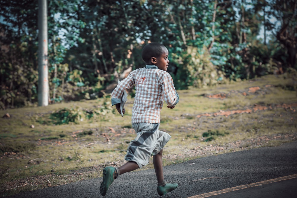 boy running on asphalt road near grass field