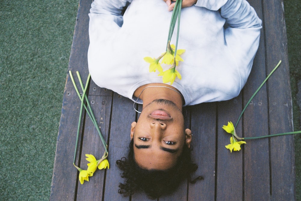 Mann liegt auf grauem Holztisch und hält gelbe Blumen in der Hand