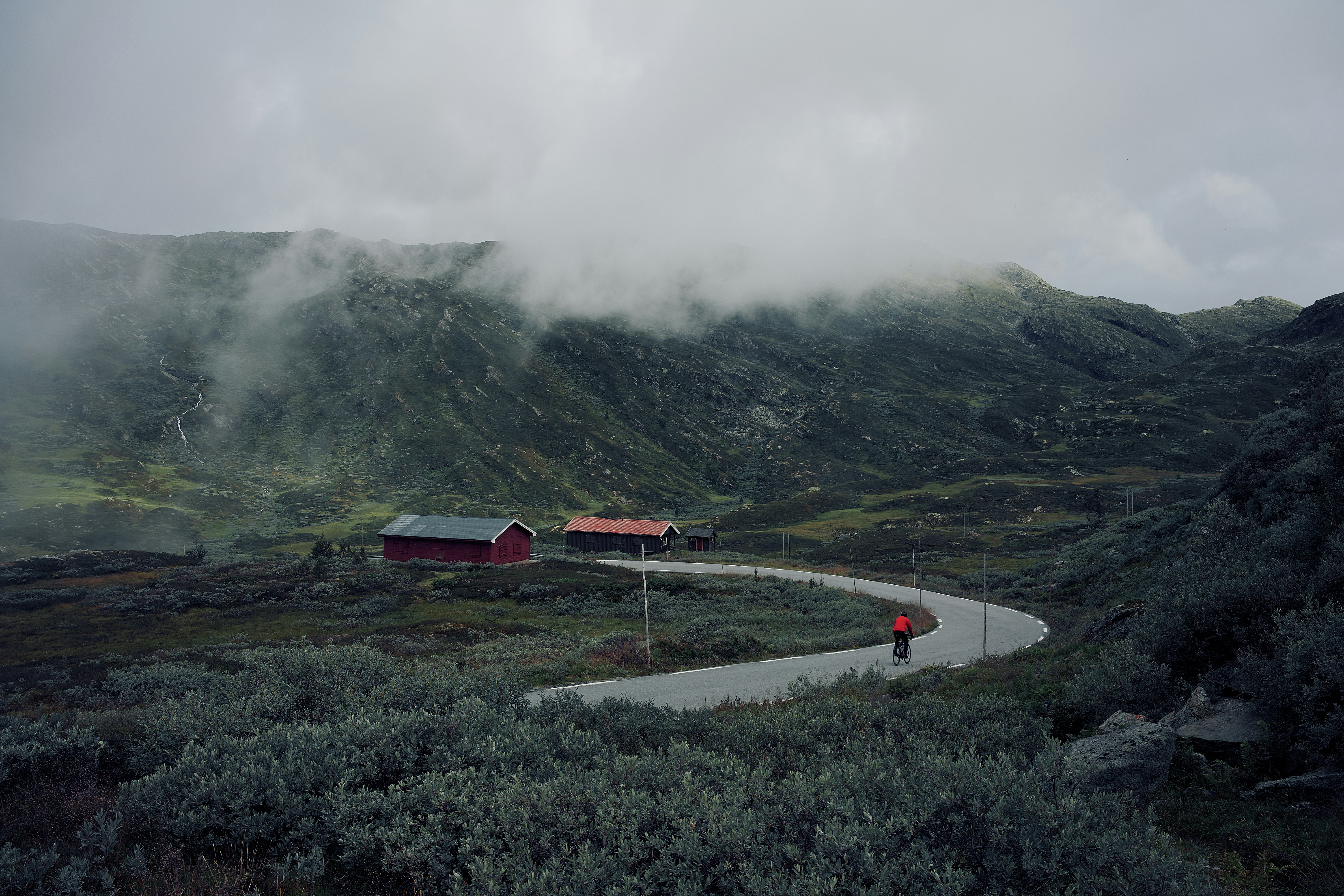 person riding bicycle going towards red and black barn during daytime