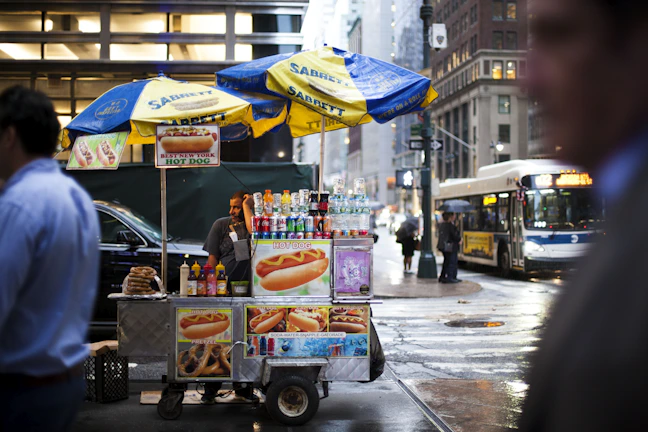 Close-up of a steaming Sabrett hotdog topped with mustard and onions on a classic New York street cart.