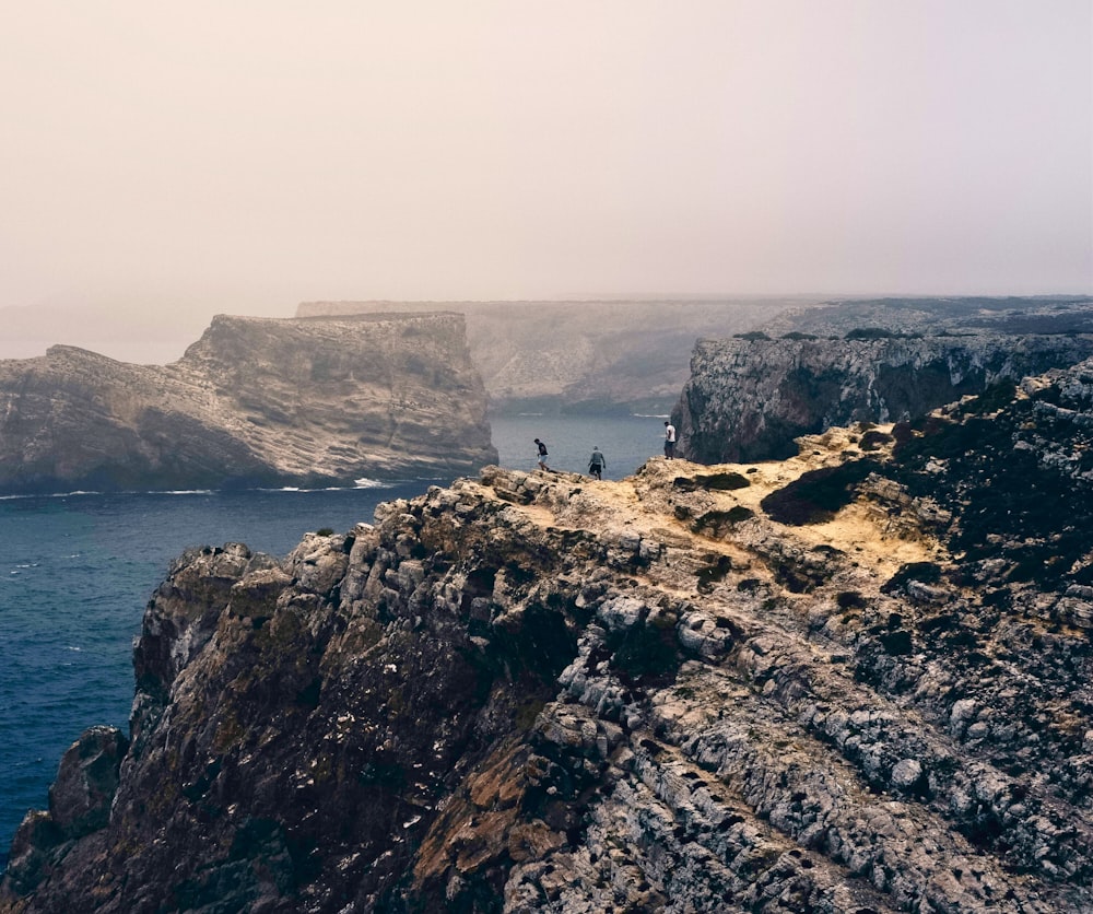 three people on cliff at daytime