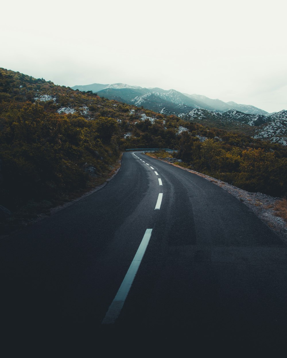 empty asphalt road leading towards rocky mountains