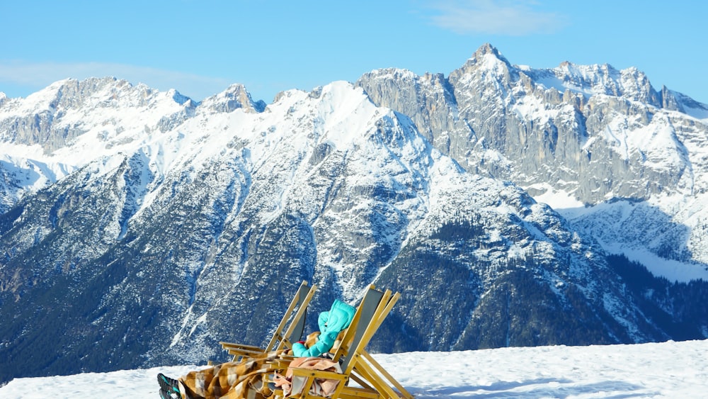 person sitting on adirondack chair on snow mountain