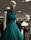 Mannequins dressed in elegant gowns on display in a retail store. One mannequin is wearing a sleeveless teal dress with ruffled shoulders, while the other is in a black lace off-shoulder gown. The store has a well-lit ceiling with numerous lights and carries a variety of clothing items visible in the background.