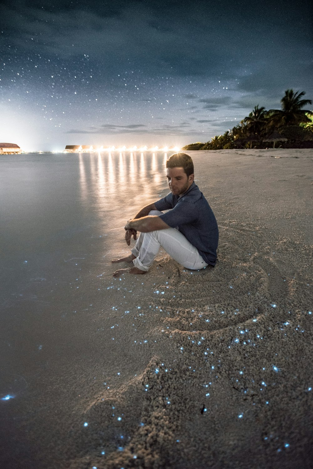 Mann sitzt auf braunem Sand neben einem Gewässer