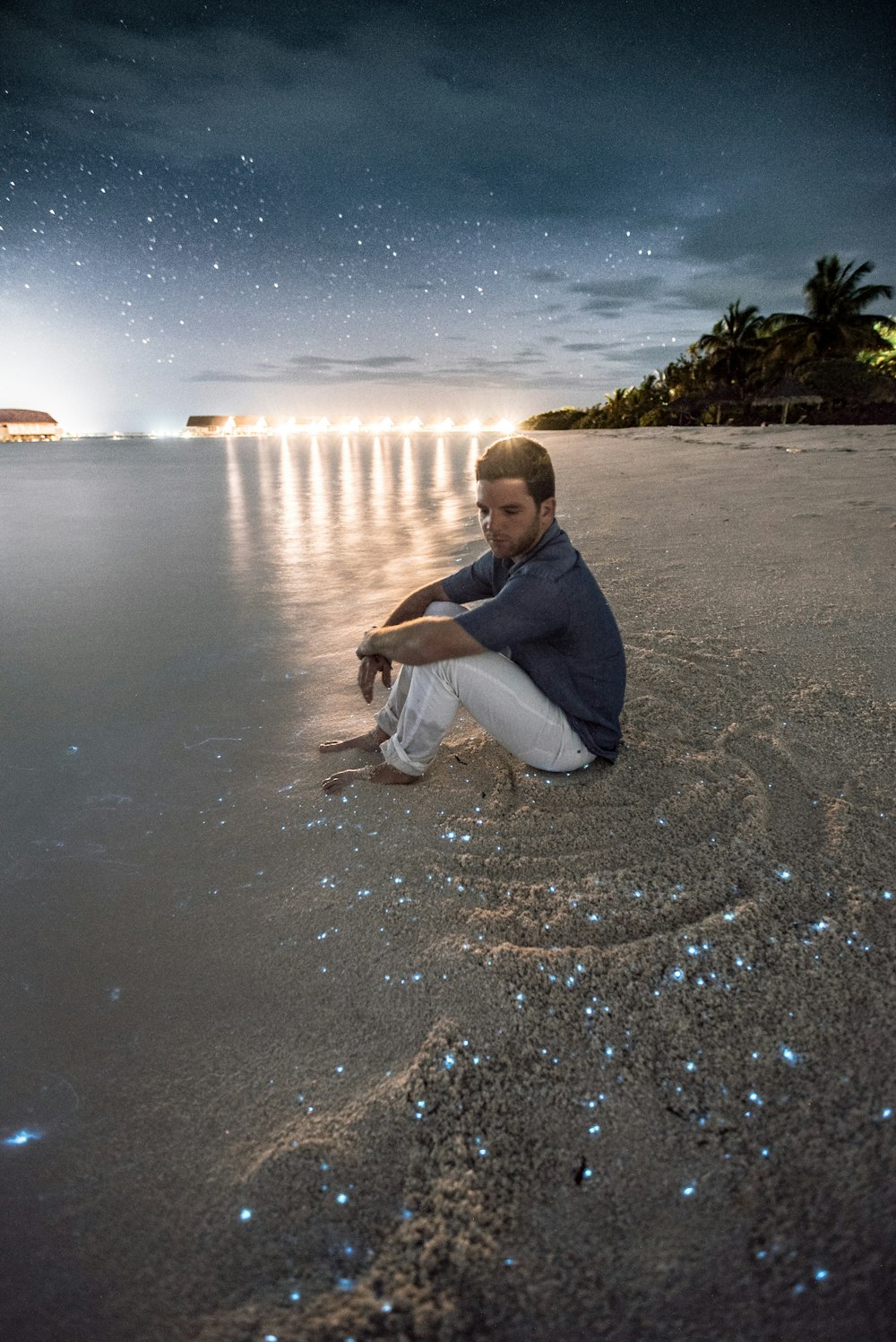 man sitting on brown sand beside body of water