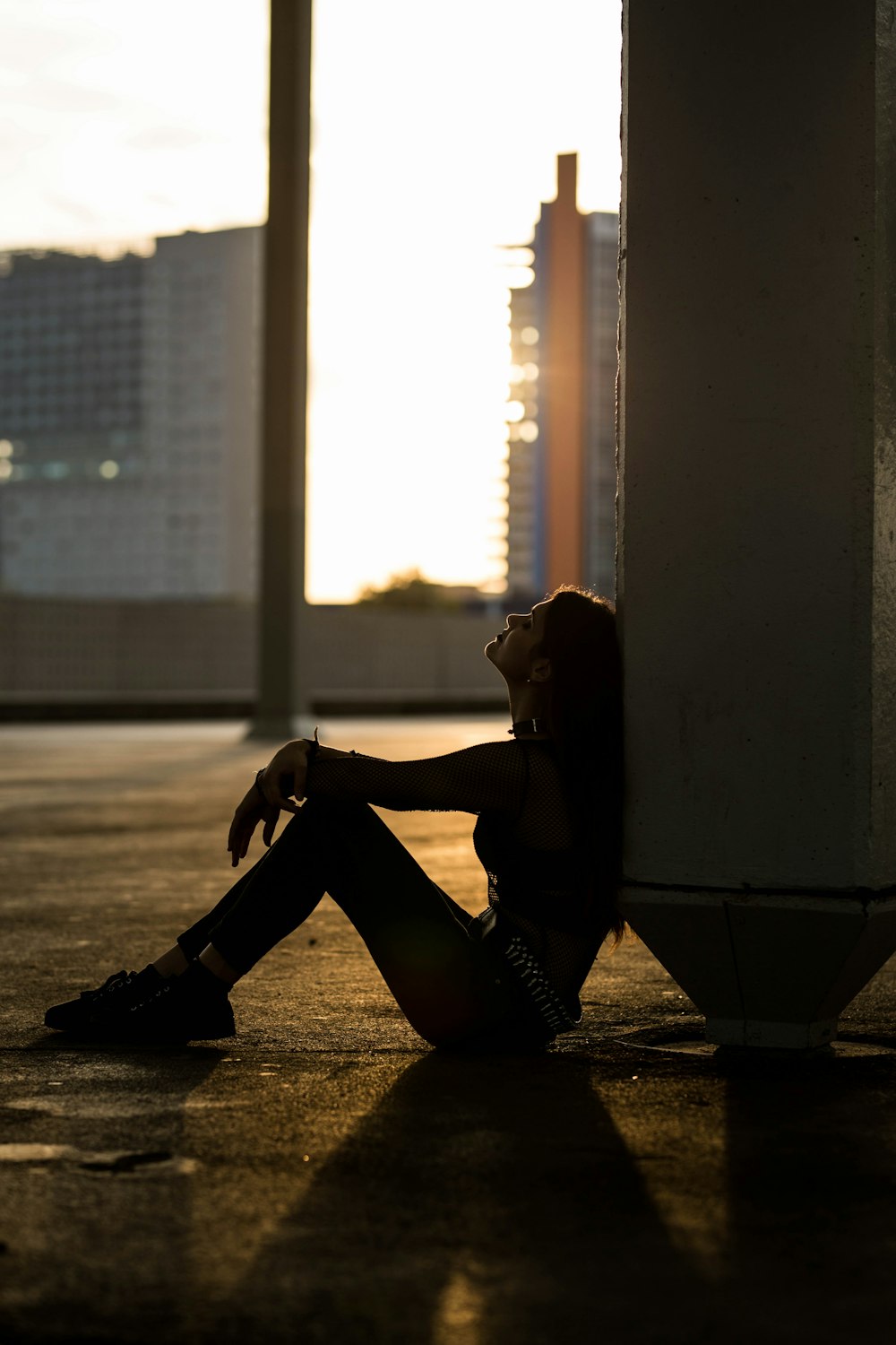 Silhouette einer Frau, die während der goldenen Stunde auf Betonpflaster sitzt