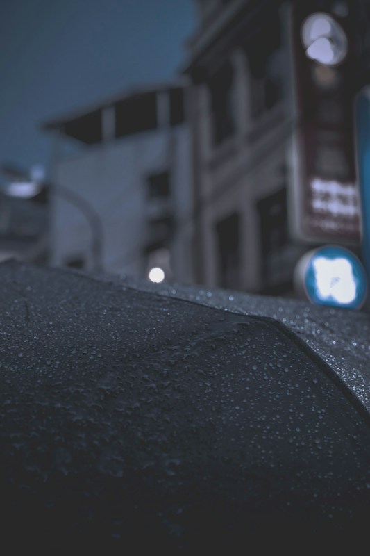 雨滴落在黑色雨傘傘面上的特寫，背景是模糊的街道