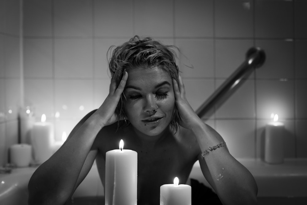 기둥 촛불 앞에서 욕조에 있는 여자의 그레이 스케일 사진