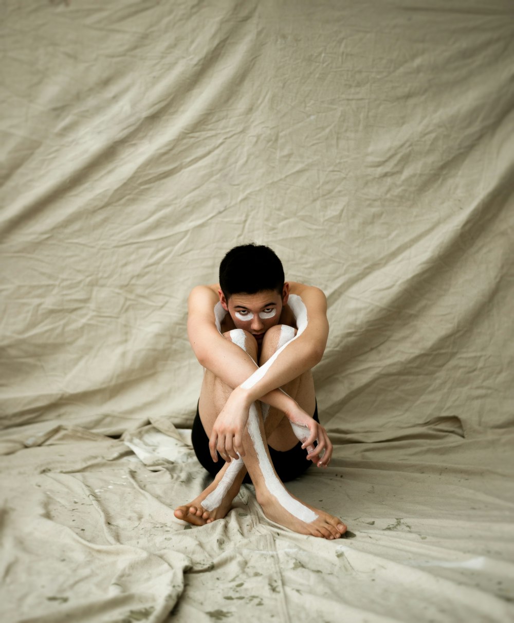 Mann sitzt auf braunem Textil und zeigt Körperbemalung