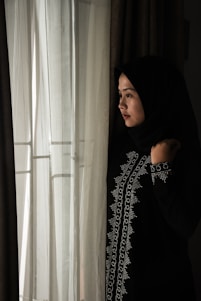 A serene photo of a woman wearing a flowing pastel abaya and hijab, standing softly lit against a minimalist background.