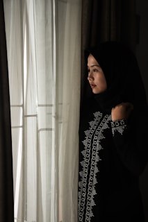 Softly lit photo of a woman wearing a flowing ivory abaya standing by a mosque arch.
