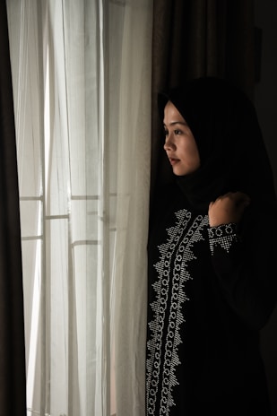 Softly lit photo of a woman wearing a flowing ivory abaya standing by a mosque arch.