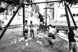 A group of kids laughing while swinging on bright yellow and orange swings under leafy canopy