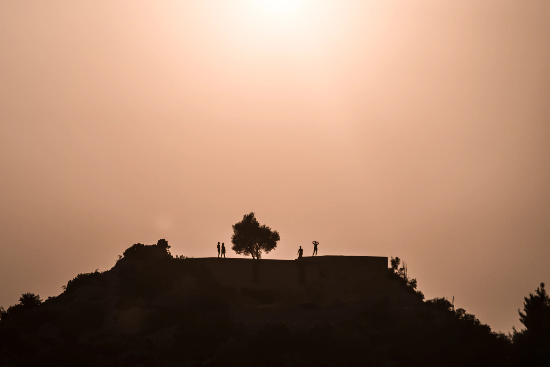 A serene sunset view from a small hilltop during a short trip, with silhouettes of travelers sharing stories.