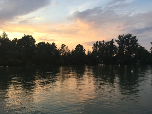 A serene lake reflecting the fiery colors of a dusk sky surrounded by trees.