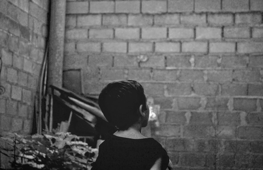 grayscale photo of boy standing near wall