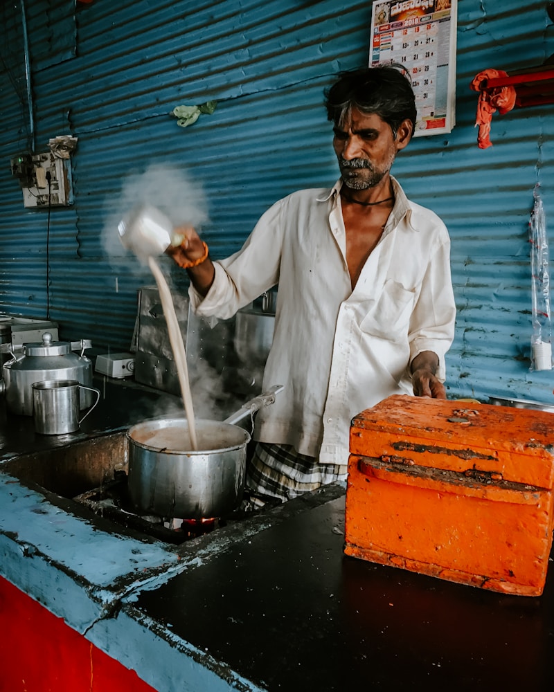 A chai vendor pouring milk into a simmering pot of spiced tea at a street stall