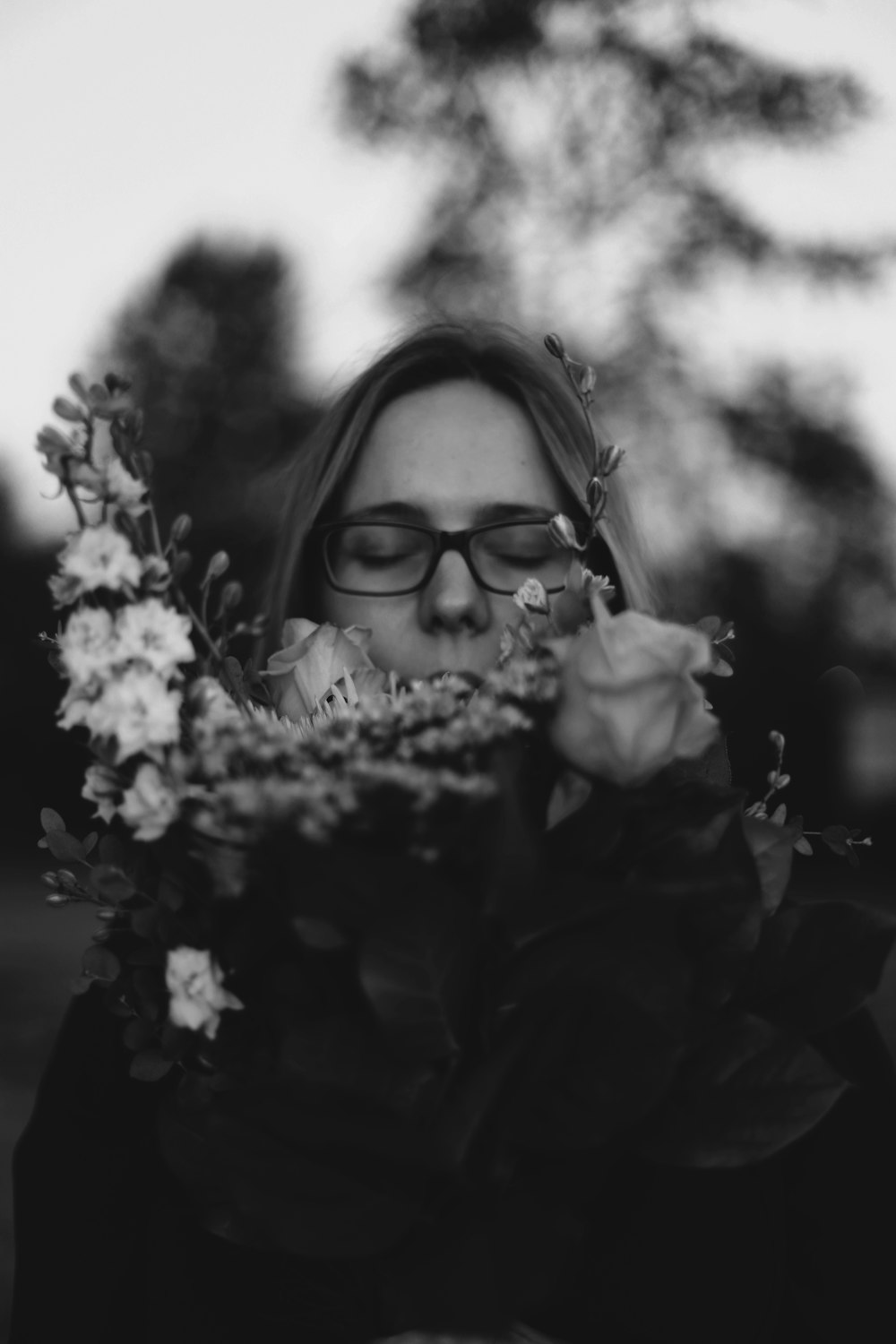 grayscale photo of woman smelling flower