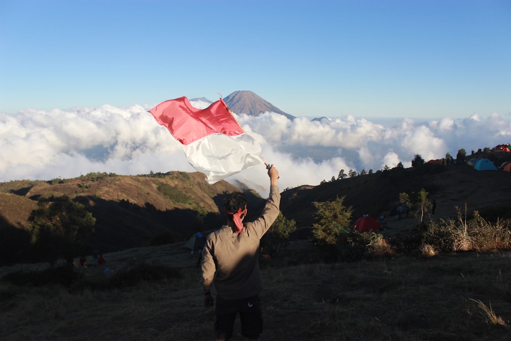 man waving red and white flag on top of mountain under clear day sky