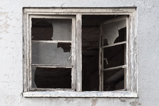 A weathered and dilapidated window with shattered glass panes against a textured, worn wall.