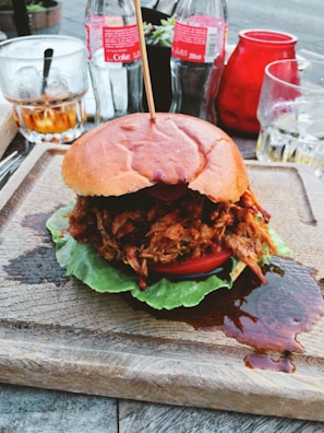 A rustic wooden table set with pulled pork sandwiches topped with coleslaw and pickles.