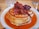 Smiling woman enjoying a stack of hot cakes with syrup and butter at a cozy breakfast table.