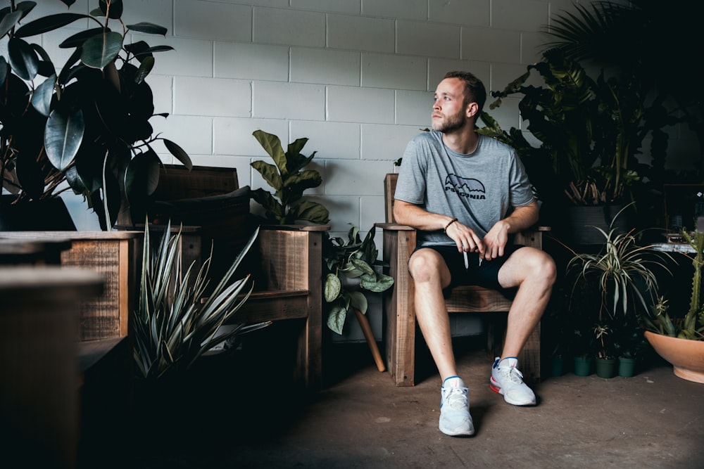 seated man between potted plants in front of while wall