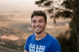 Man in a blue shirt on a naturey hill smiling