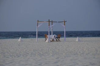 A serene beach scene featuring a family relaxing on a foldable picnic mat with a compact aluminum table and moon chairs set up nearby.