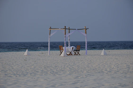 A serene beach scene featuring a family relaxing on a foldable picnic mat with a compact aluminum table and moon chairs set up nearby.