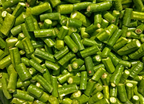 A close-up view of numerous chopped green beans. The fresh beans are uniformly cut into short segments, displaying a vibrant green color and a glossy texture that suggests they are freshly washed.