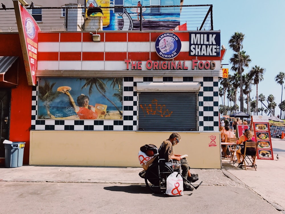 man sitting on wheel chair beside The Original Food store during daytime