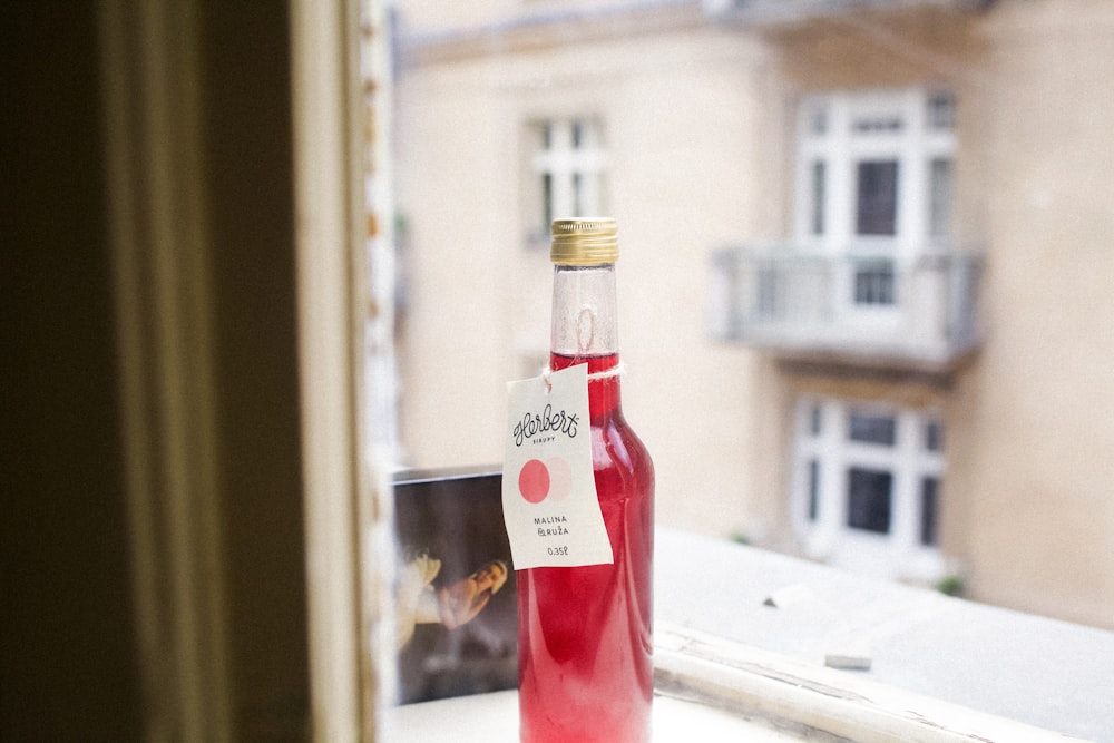 Selektive Fokusfotografie einer mit roter Flüssigkeit gefüllten Flasche auf der Fensterbank