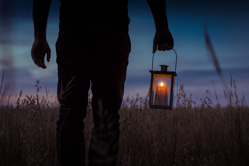 Foto da silhueta do homem carregando a lanterna da vela com a vela acesa