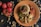 A plate with a culinary presentation consisting of couscous topped with mushrooms and tomato sauce, surrounded by peas and slices of roasted vegetables garnished with sesame seeds and cashews. The table is adorned with whole tomatoes and scattered cashew nuts.
