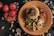 A plate with a culinary presentation consisting of couscous topped with mushrooms and tomato sauce, surrounded by peas and slices of roasted vegetables garnished with sesame seeds and cashews. The table is adorned with whole tomatoes and scattered cashew nuts.