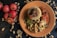 A plate with a culinary presentation consisting of couscous topped with mushrooms and tomato sauce, surrounded by peas and slices of roasted vegetables garnished with sesame seeds and cashews. The table is adorned with whole tomatoes and scattered cashew nuts.